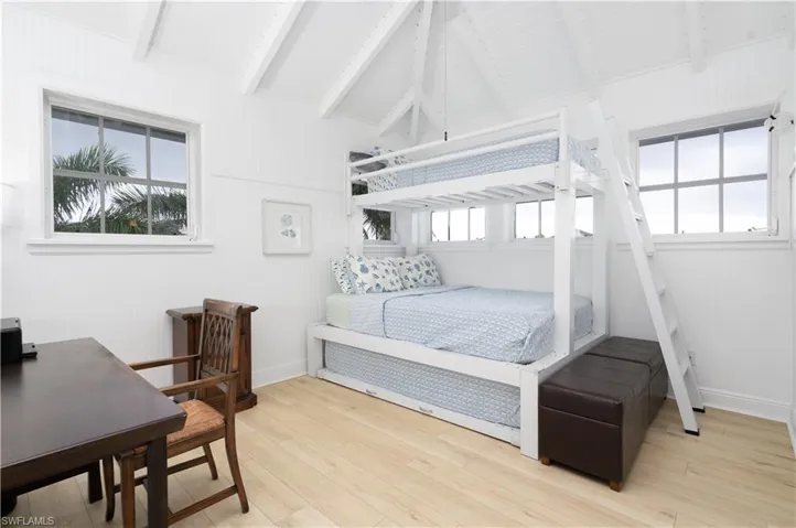Loft bedroom with light wood-style floors, multiple windows, and wooden walls