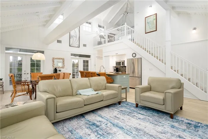Living area featuring beamed ceiling, french doors, high vaulted ceiling, stairs, and light wood-style flooring