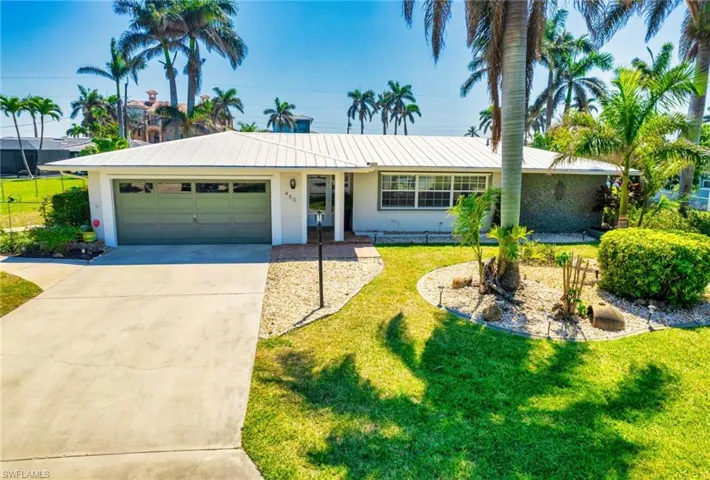 Ranch-style home with stucco siding, concrete driveway, front lawn, a 2 car garage, and metal roof and palm trees