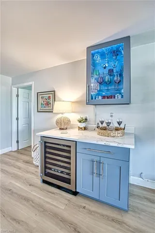 Bar featuring wine cooler, light wood finished floors, and a glass display cabinet with lights and storage