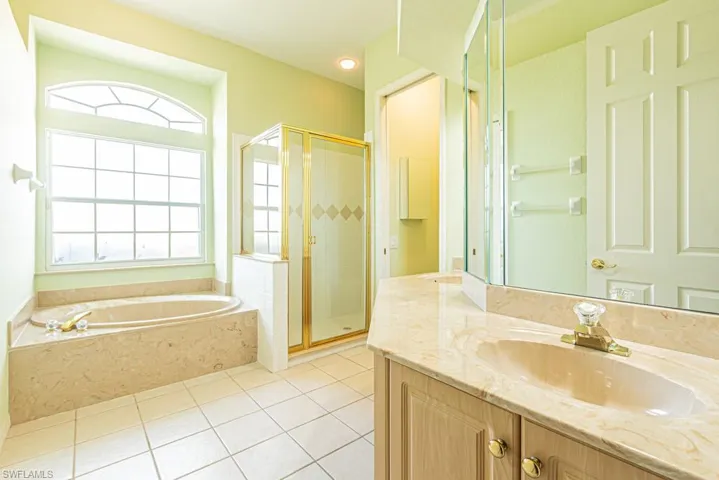 Full master bathroom with a stall shower, vanity with dual sinks, a bathtub, and light tile patterned floors.
