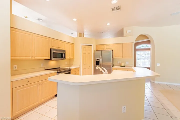 Kitchen with light countertops, a center island with sink, stainless steel appliances, light wood finish cabinets, and light tile patterned flooring