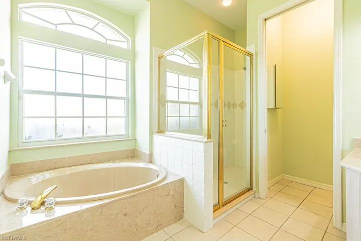 Full bathroom featuring a shower stall, a garden tub, light tile patterned flooring, and vanity with dual sinks.