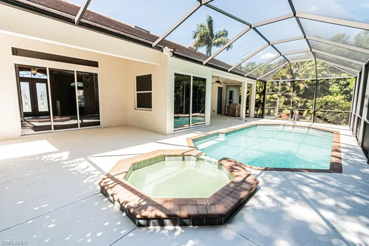 Relaxing pool / spa with glass enclosure, a sunroom, and a patio