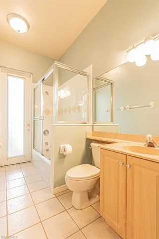 Bathroom with light tile patterned flooring, vanity, and bath / shower combo with glass door