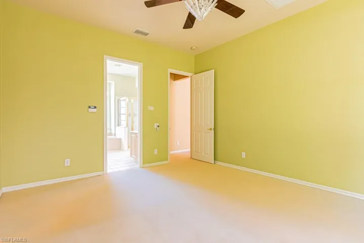 Large master bedroom with light colored carpet, a ceiling fan, and connected bathroom.