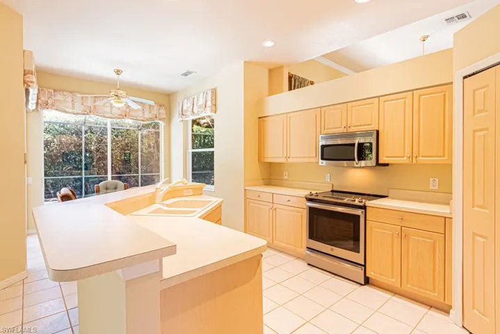 Kitchen featuring stainless steel appliances, light countertops, a kitchen island with sink, light tile patterned flooring, and ceiling fan