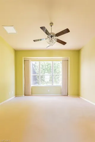 Master bedroom with light colored carpet and a ceiling fan and large windows.