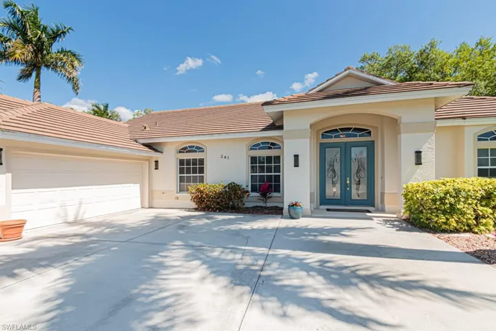 View of front facade featuring a tile roof, concrete driveway, French front doors, an attached three car garage.