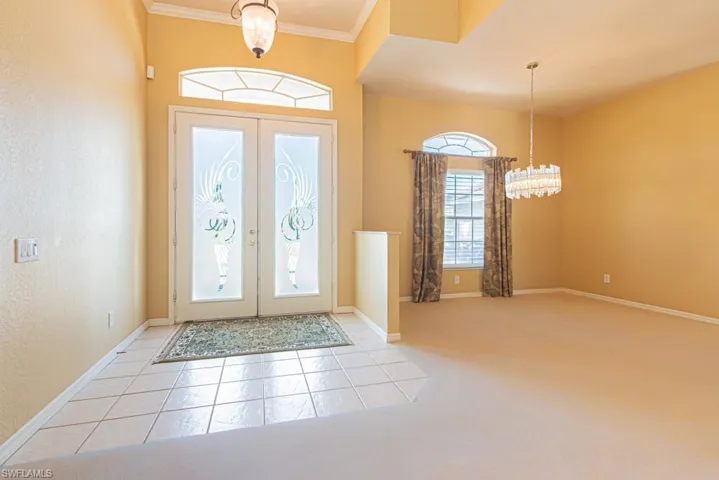 Foyer with hanging lights, light tile patterned floors, light ornamental molding, and french doors