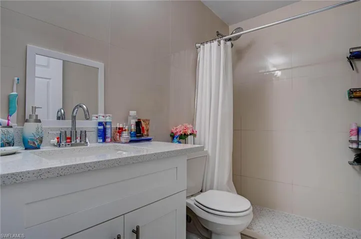 Bathroom featuring tile walls, walk in shower, toilet, and vanity