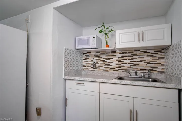 Kitchen with white cabinetry, backsplash, and sink