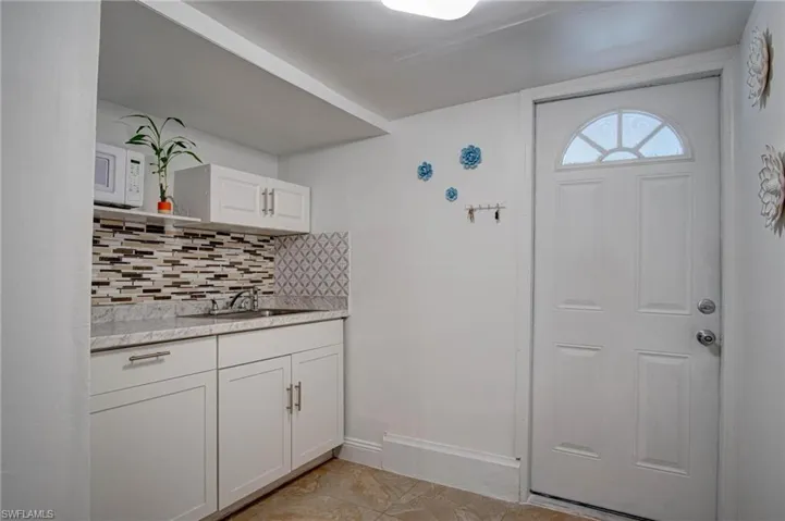 Kitchen featuring white cabinets, tasteful backsplash, sink, white microwave, and light tile patterned flooring