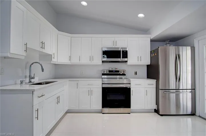 Kitchen featuring white cabinetry, vaulted ceiling, sink, appliances with stainless steel finishes, and light tile patterned flooring