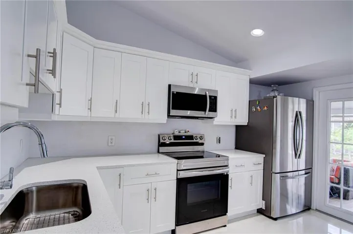 Kitchen with lofted ceiling, sink, appliances with stainless steel finishes, and white cabinets
