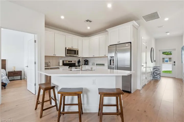 Contemporary kitchen featuring white cabinetry, stainless steel appliances, a white tile backsplash, and light wood-finish flooring