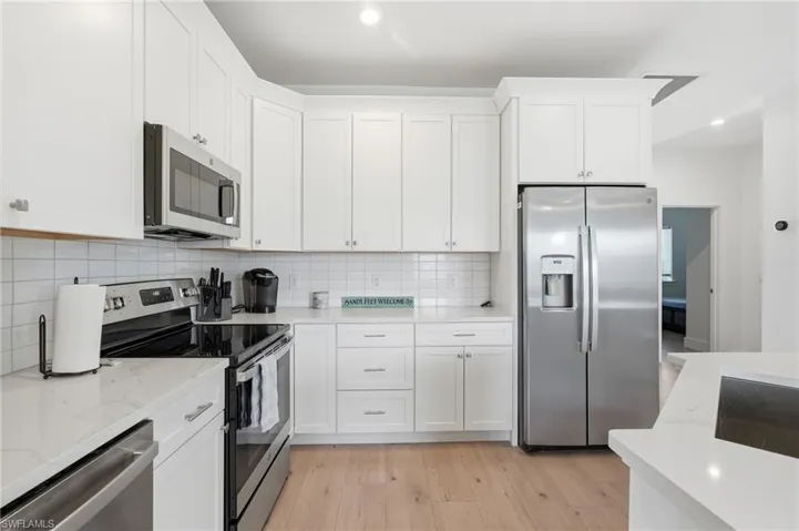 Kitchen featuring white shaker cabinetry, stainless steel appliances, light wood-finish flooring, white subway tile backsplash, and light-toned countertops