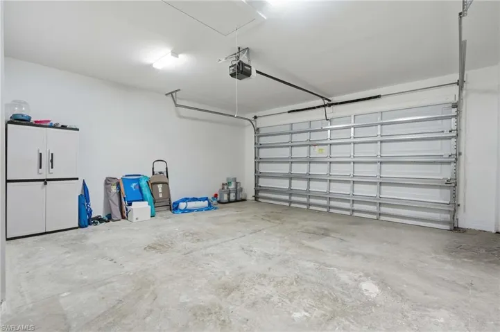 Spacious garage featuring a concrete floor, white walls, overhead lighting, and an automatic garage door opener