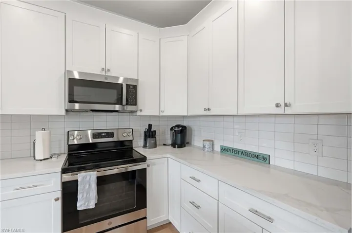 Kitchen featuring white cabinetry, stainless steel appliances, a white subway tile backsplash, and light-toned countertops