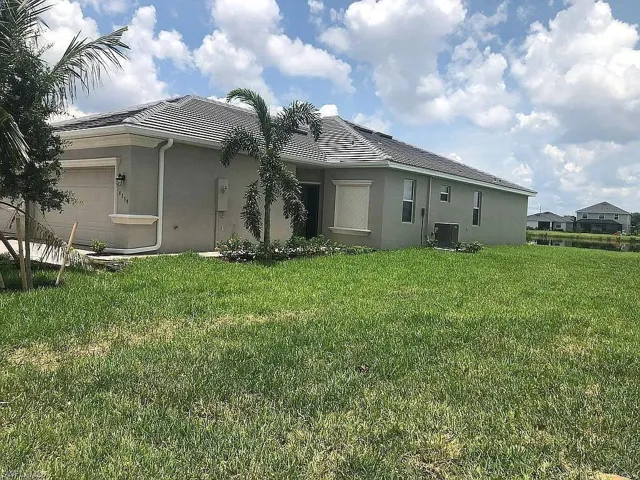 Stucco exterior with a tiled roof, integrated garage, and landscaped front garden beds featuring palm trees