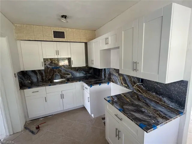 Kitchen with backsplash, a sink, visible vents, and white cabinets