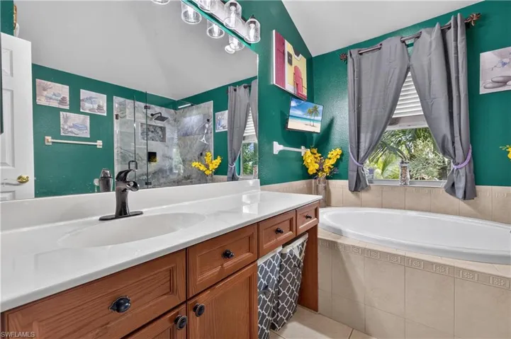 Bathroom featuring a built-in soaking tub, a stand-up shower with glass enclosure, a vanity with a white countertop and wood-finish cabinetry, and a window with natural light