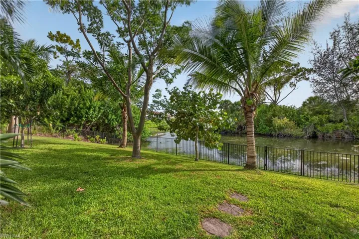 Lush green lawn with mature trees and stepping stones, featuring a black metal fence bordering a natural waterway