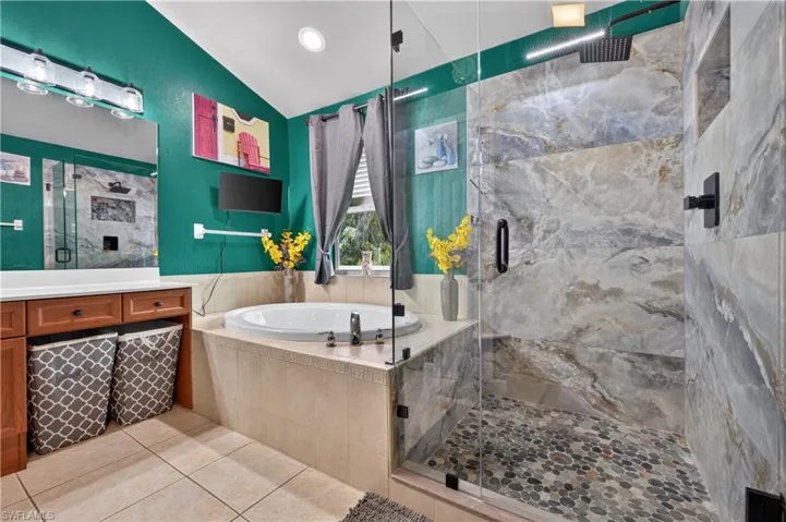 Bathroom featuring a spacious walk-in shower with a glass enclosure, large format stone-finish tile, and a pebble-stone floor