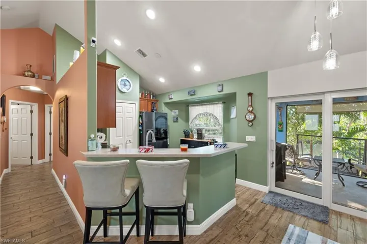 Kitchen with a counter-height breakfast bar featuring a solid surface countertop, wood-finish flooring, and vaulted ceilings