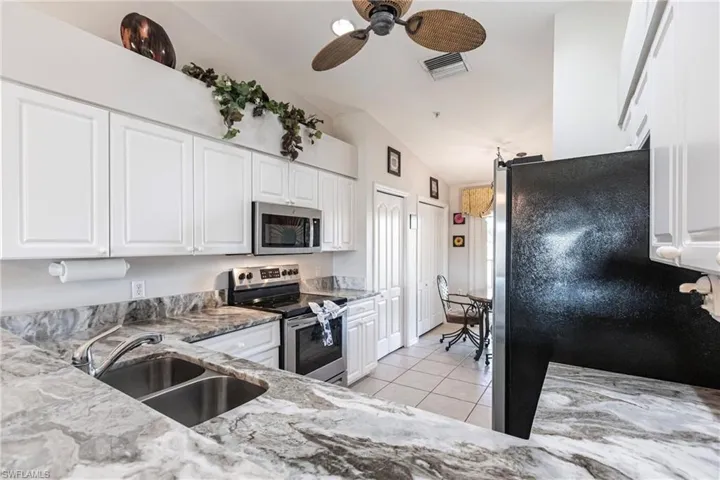 Kitchen with white cabinetry, sink, light stone counters, lofted ceiling, and appliances with stainless steel finishes