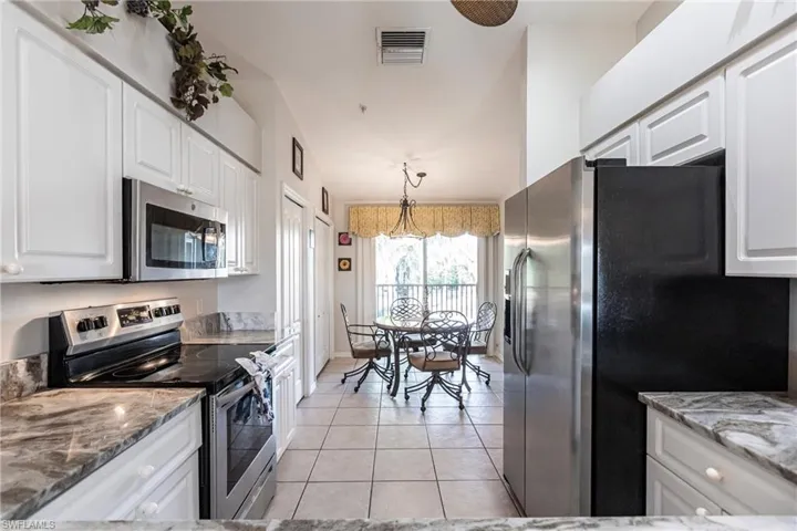 Kitchen with appliances with stainless steel finishes, light stone counters, light tile patterned floors, decorative light fixtures, and white cabinetry
