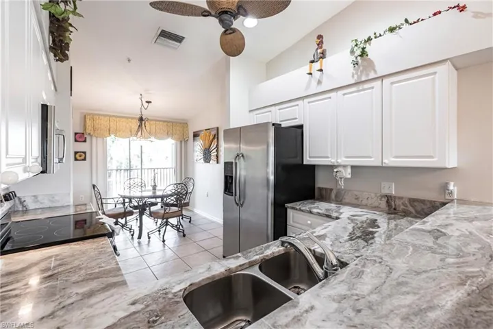 Kitchen with light stone countertops, white cabinetry, sink, ceiling fan, and stainless steel appliances