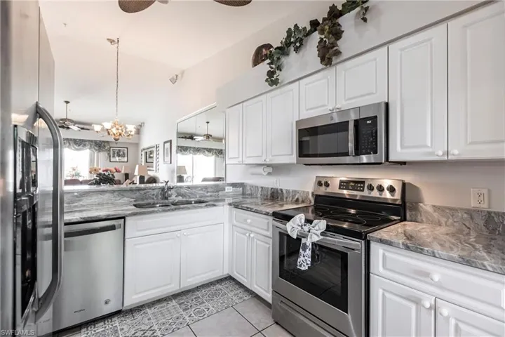 Kitchen featuring appliances with stainless steel finishes, sink, white cabinets, a chandelier, and light tile patterned flooring