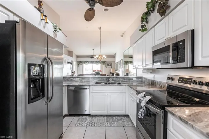 Kitchen with appliances with stainless steel finishes, light stone counters, sink, light tile patterned floors, and white cabinetry