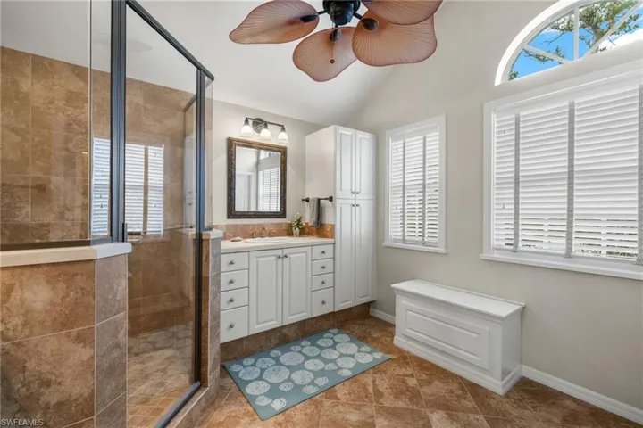 Bathroom featuring tile patterned floors, vanity, ceiling fan, a shower with door, and lofted ceiling