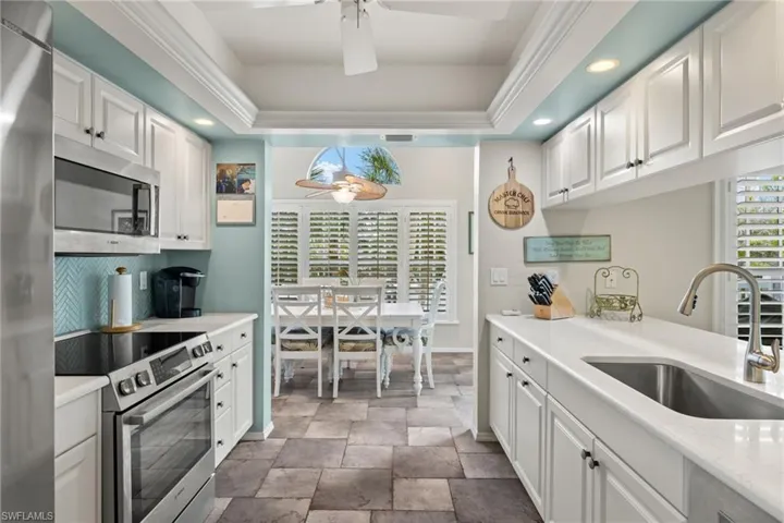 Kitchen featuring ceiling fan, appliances with stainless steel finishes, sink, white cabinets, and a tray ceiling