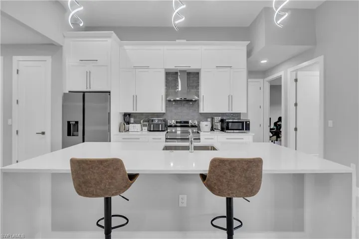 Kitchen with white cabinetry, appliances with stainless steel finishes, tasteful backsplash, wall chimney exhaust hood, and a spacious island