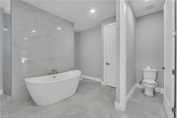 Bathroom featuring tile walls, a freestanding tub, light marble finish flooring, and recessed lighting