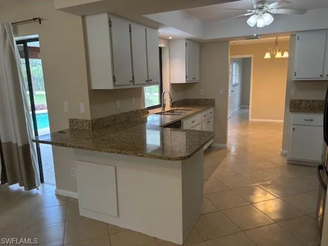 Kitchen featuring kitchen peninsula, light tile patterned flooring, ceiling fan with notable chandelier, and white cabinets