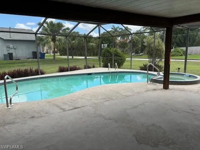 View of pool with a patio area, a lawn, and glass enclosure