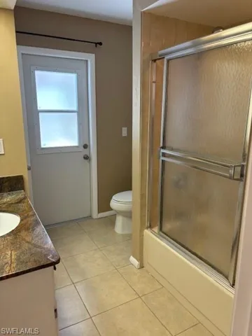 Full bathroom featuring vanity, tile patterned floors, combined bath / shower with glass door, and toilet