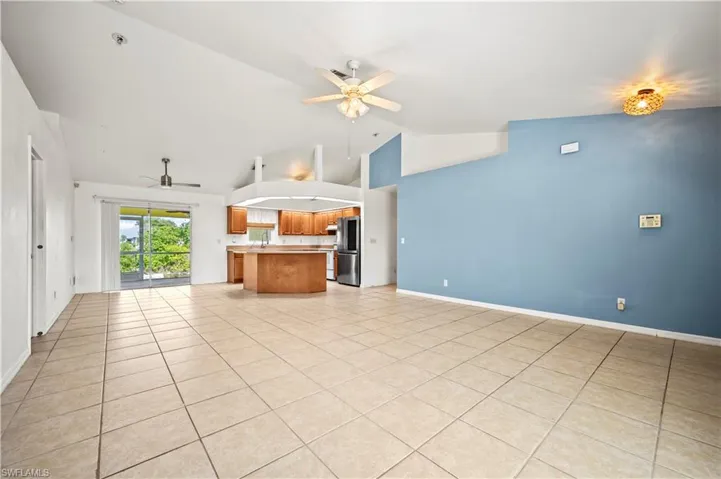 Unfurnished living room featuring a ceiling fan, light tile patterned floors, high vaulted ceiling, and baseboards