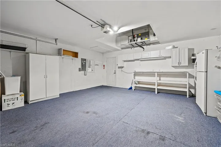 Garage featuring freestanding refrigerator, electric panel, and a garage door opener