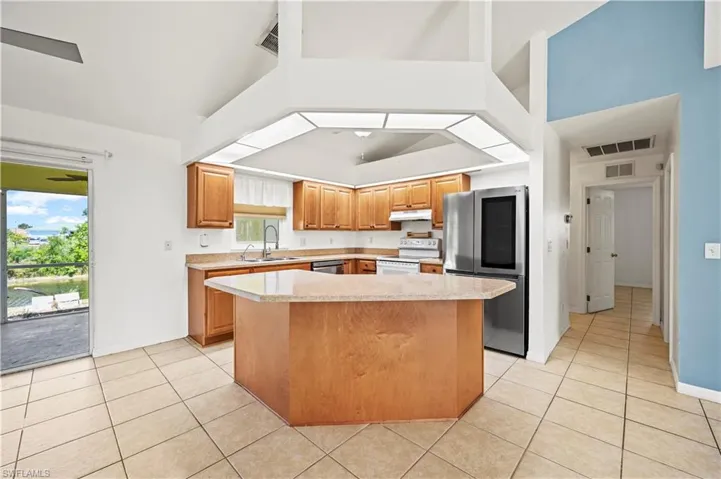 Kitchen featuring appliances with stainless steel finishes, a sink, light countertops, light tile patterned floors, and a center island