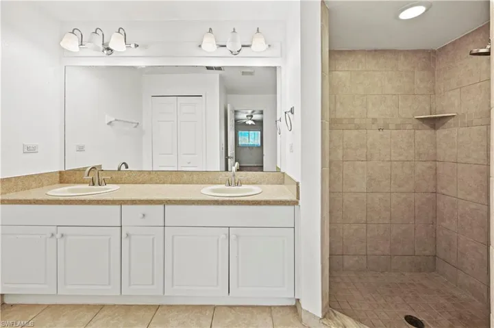 Bathroom featuring double vanity, tile patterned floors, and tiled shower