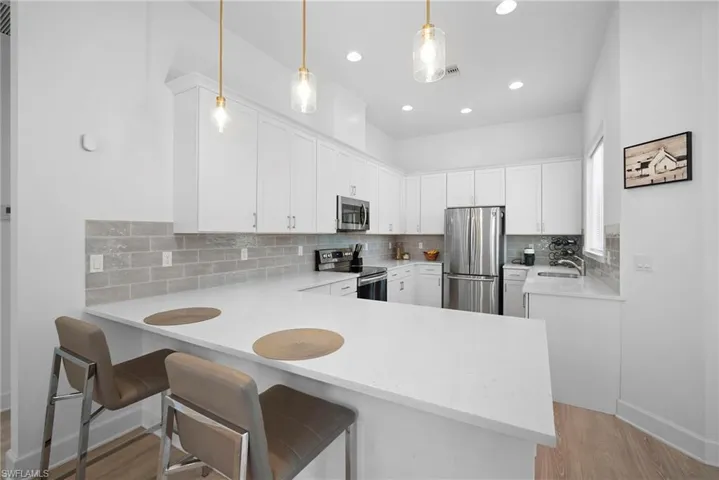 Kitchen with tasteful backsplash, stainless steel appliances, a breakfast bar area, light wood-style floors, and light stone countertops