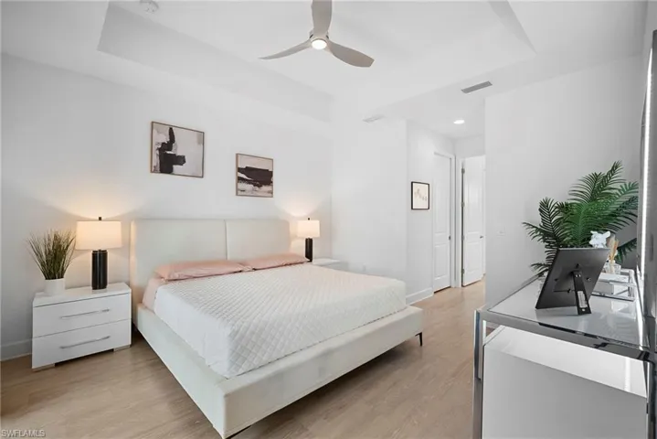 Bedroom with a tray ceiling, light wood-style flooring, a ceiling fan, and recessed lighting