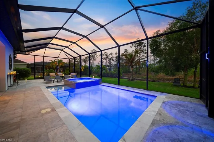 Pool at dusk featuring a sunroom, a pool with connected hot tub, a lanai, a yard, and a patio area