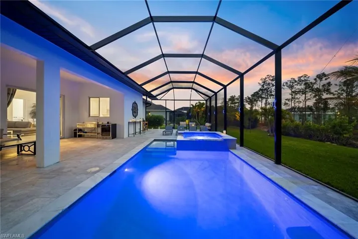 Pool at dusk with exterior kitchen, a yard, a pool with connected hot tub, a lanai, and a sunroom
