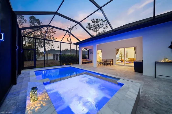 Pool at dusk with an outdoor pool, a sunroom, an in-ground hot tub, and a patio
